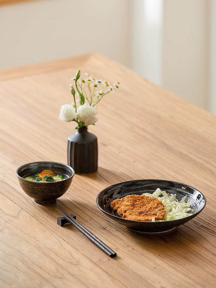 Retro Japanese ceramics featuring exquisite plate designs on a wooden table, accompanied by a small vase with flowers.