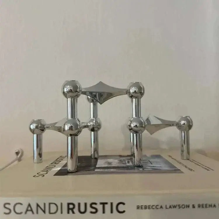 Metal sculptural candle holder with modular arms and polished finish on a table.