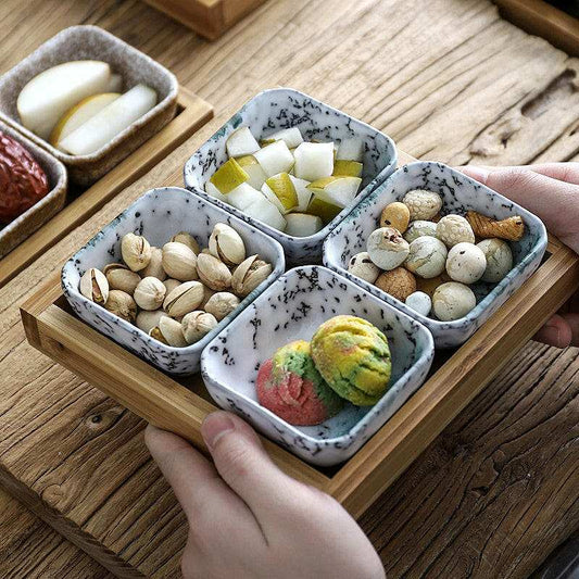 Ceramic bowls on bamboo tray for snacks.