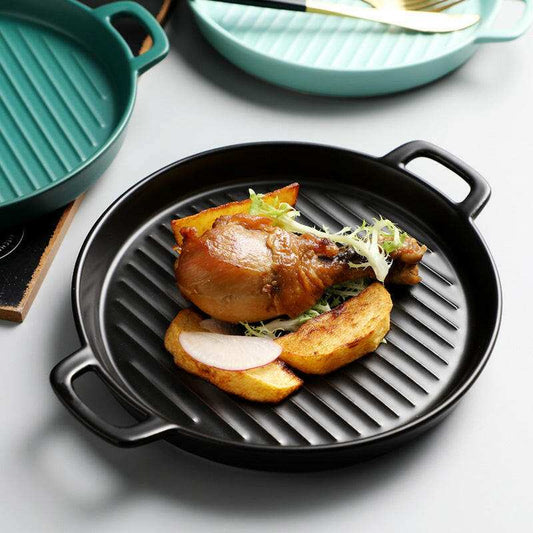 Round black grill plate with handles, ideal for baking and grilling.