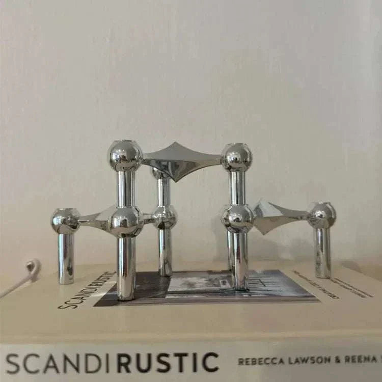 Metal sculptural candle holder with modular arms and polished finish on a table.