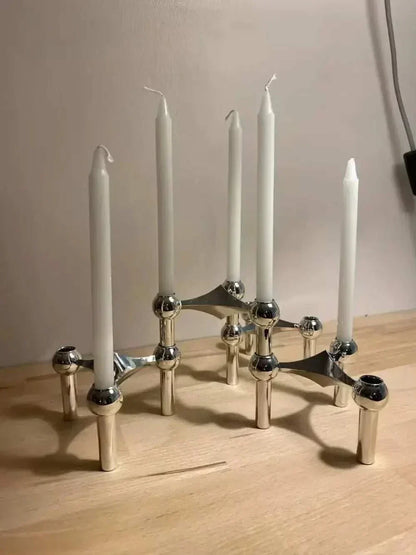 Modern metal sculptural candle holder with modular arms and elegant candles on a wooden surface.