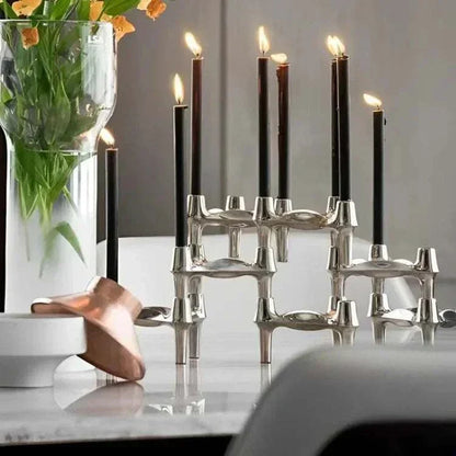 Metal sculptural candle holder with modular arms and elegant candles on a table.